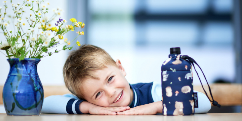 Junge mit der Glas-Trinkflasche auf dem Schreibtisch